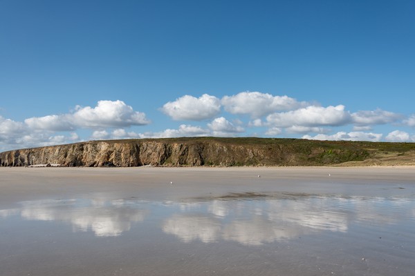 Falaises et sable fin de la plage de Kersiguénou sur la presqu'île de Crozon sous un ciel bleu